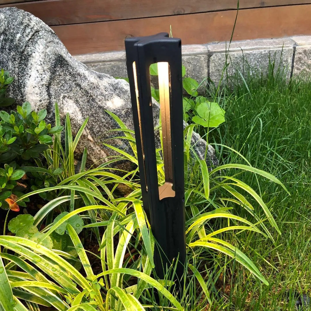 Black garden tool leaning against a rock with green plants in the background